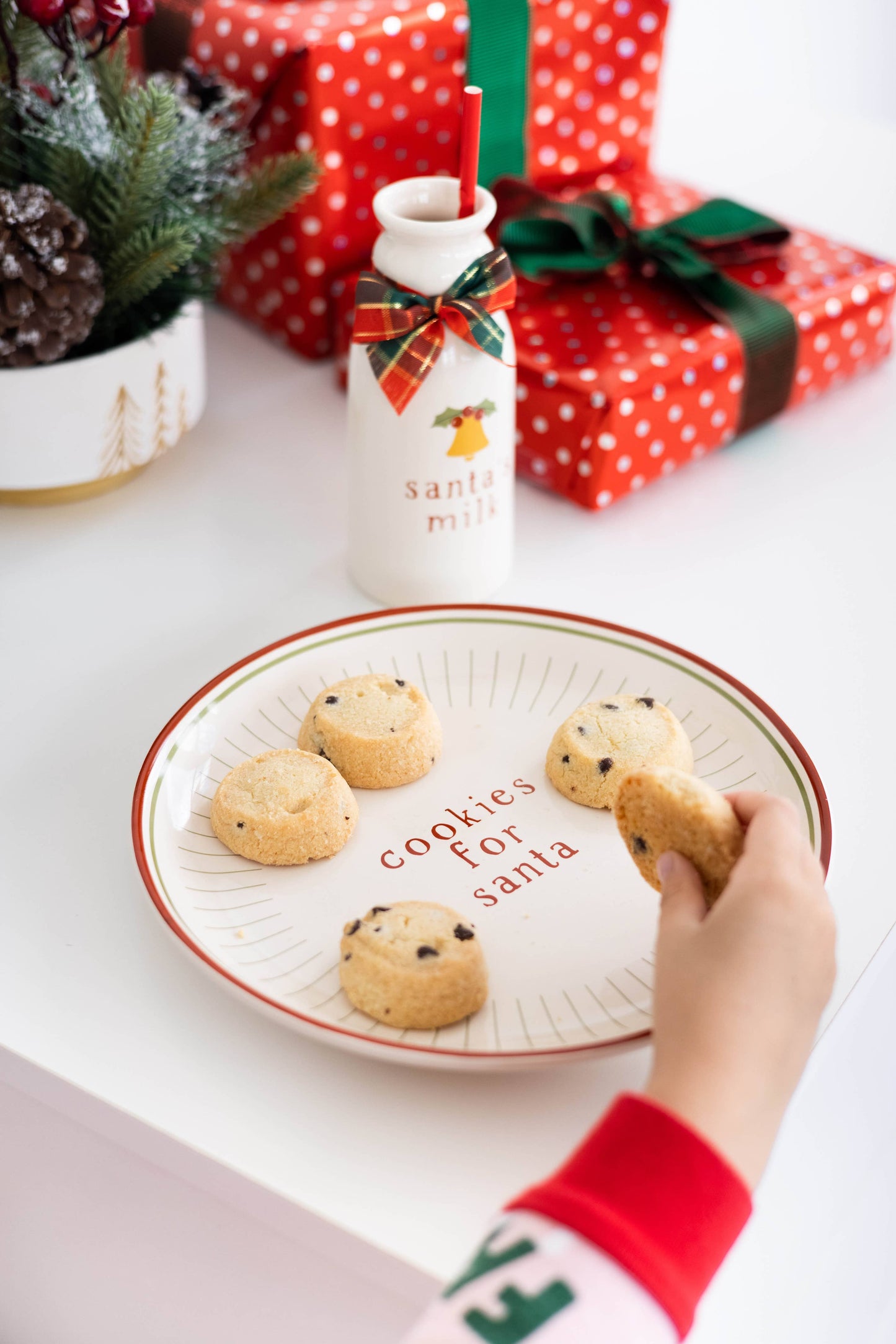 Cookies on a plate with 'Cookies for Santa' text, next to a bottle labeled 'Santa Milk', with Christmas presents and decorations in the background.