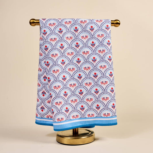 Towel with American flag pattern hanging on a gold towel rack against a beige background