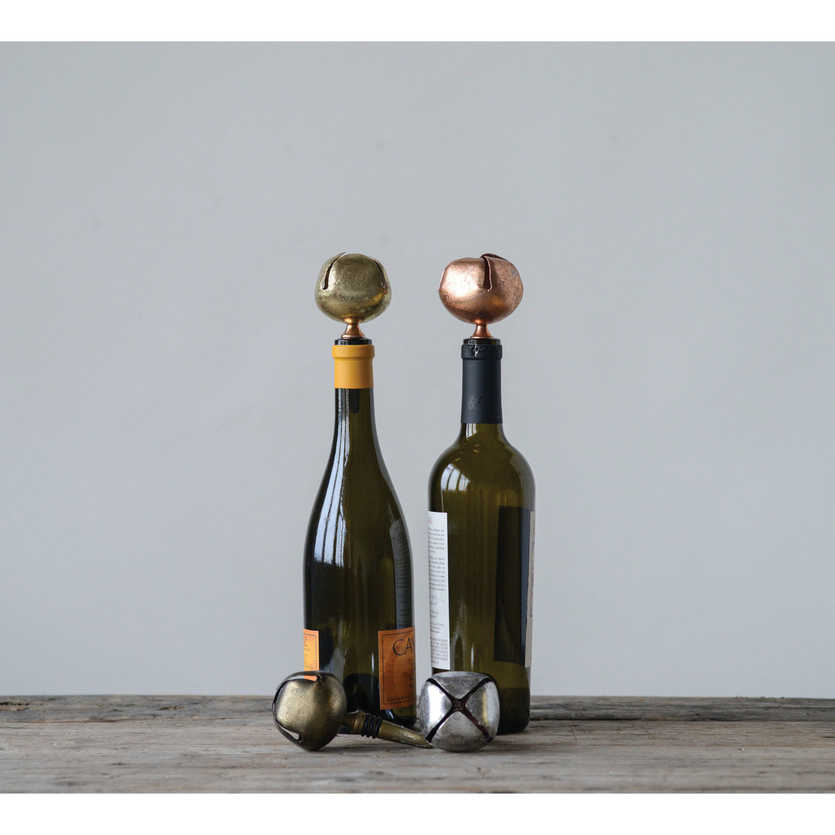 Two wine bottles with decorative bottle stoppers on a wooden surface against a light gray background