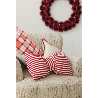 Red and cream striped velvet bow pillow styled on a neutral armchair with festive Christmas pillows and a red holiday wreath.
